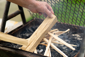 A man light a fire on an outdoor grill using wood sticks, preparing fire for a barbecue. garden setting.