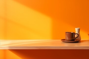 Brown cup with plate and vase on wooden desk front orange wall background.
