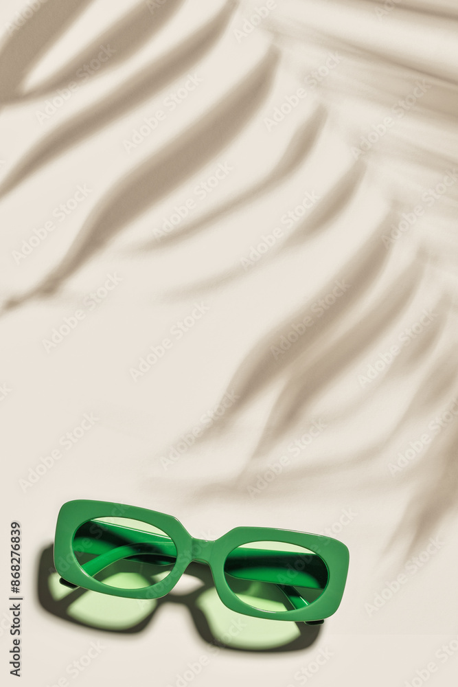 Wall mural Green Sunglasses on beige colored background at sunlight with palm leaf shadow, summer plastic-framed glasses. Aesthetic top view eyeglasses, fashion eyewear, minimal trend, copy space, pastel