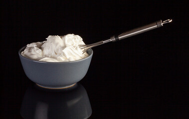 Ceramic bowl with whipped cream with a metal whisk. Isolated on black background...