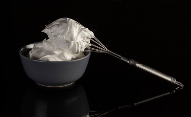 Ceramic bowl with whipped cream with a metal whisk. Isolated on black background.