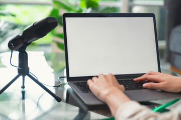 Woman hand type on the keyboard on laptop with mockup of blank screen and microphones for record podcast interview for radio.