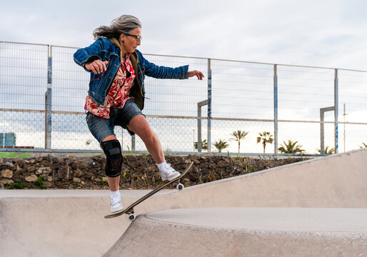 A graceful and assured senior woman with silver hair skateboarding in the open air.