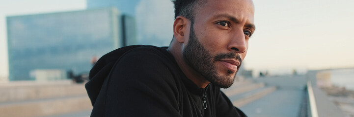 Obraz premium Young bearded male athlete standing on the embankment looking at the sea, panorama