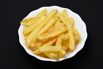 French fries in a white plate on a black background. Delicious fried potatoes.