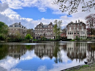 Naklejka premium Reflective Waters of Vondelpark: Historic Amsterdam houses reflect beautifully on the calm waters of Vondelpark, blending architecture with nature.