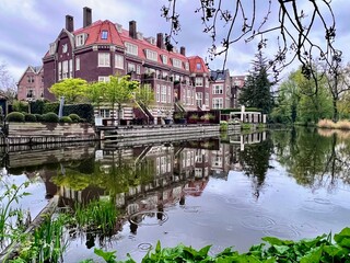 Reflections of Elegance: Mirror-like reflections of elegant Amsterdam houses in a Vondelpark pond, surrounded by fresh spring greenery and a serene atmosphere.