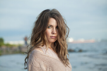 Nice young adult woman with natural make-up and long wavy brown hair on blue sea beach outdoor portrait