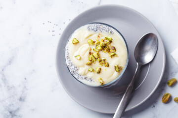Chia pudding with white chocolate and pistachio in glass, white marble background. Healthy breakfast recipe concept.