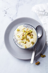 Chia pudding with white chocolate and pistachio in glass, white marble background. Healthy breakfast recipe concept.