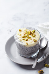 Chia pudding with white chocolate and pistachio in glass, white marble background. Healthy breakfast recipe concept.