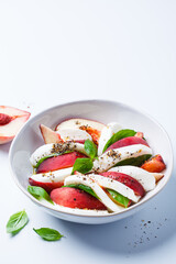 Caprese salad with peach, basil and mozzarella, white background.