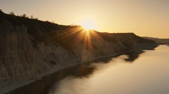 Rocky cliff coast of Cretaceous and Paleogene deposits above the sea. The sun's rays break through on the horizon. Soft sunlight reflected in the water