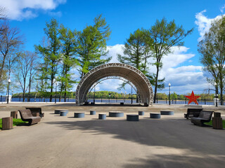 In the city park on the embankment there is a concert stage with a semicircular roof against the blue sky. © Sofya