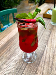 Experience the bold flavors of a spicy red cocktail with fresh basil and chili garnish, set on a rustic wooden table. Perfect for vibrant culinary photography