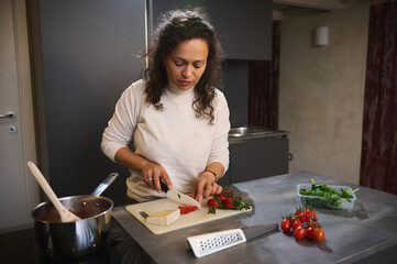 Woman cooking dinner, chopping tomatoes on cutting board. Fresh organic ingredients and veggies on...