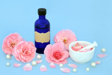 Rose flower aromatherapy essential oil preparation with pink flowers and pearls on blue. Natural...