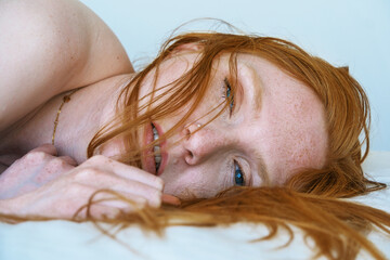 sexy red-haired woman lies her side, close-up, her hair partially covering her face, blue eyes gaze...