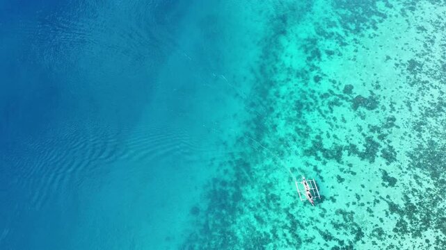 fishing boat sailing over a coral reef in the crystal clear water of the ocean aerial view