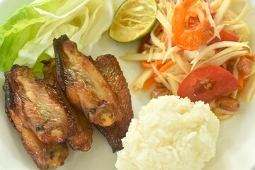 Som tum Thai spicy green papaya salad with roasted chicken wing eat couple sticky rice on plate 