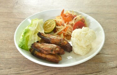 Som tum Thai spicy green papaya salad with roasted chicken wing eat couple sticky rice on plate 