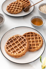 Homemade oatmeal and chia seed waffles on a white plate, accompanied by honey and ingredients