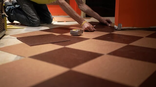 Two hands putting a vinyl composition tile, VCT into place on a kitchen floor in a home renovation project.