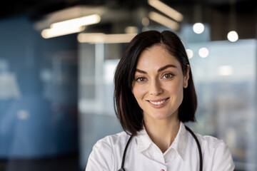 Confident female doctor with stethoscope smiling at camera in modern medical office. Professional...