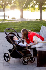Young mother with her cute baby is sitting on a park bench