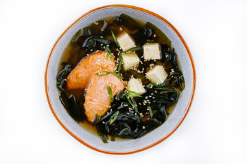 Japanese miso soup with salmon, tofu and seaweed in a bowl on a dark background. Top view.