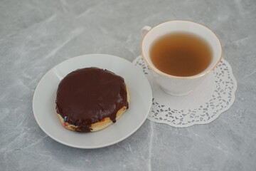 Donut with chocolate glaze and cup of tea on the table
