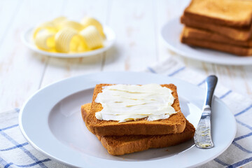 Butter and crispy pieces of toast for breakfast over white kitchen table, selective focus.