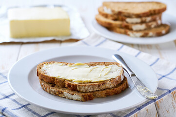 Fresh crusty buttered rye bread slices with butter  on a wooden table