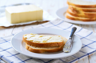 spreading butter on to wheat bread slices on a white wooden table.