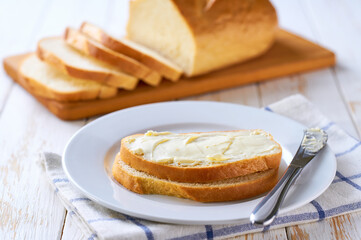 Delicious white wheat bread and fresh butter on a light wooden table, selective focus.