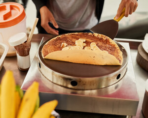 Vendor, hands and street food with crepe, banana and chocolate for Thailand road snack. Small...