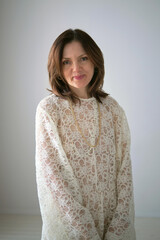 A woman in a white lace dress gazes softly at the camera, exuding warmth and elegance. The...