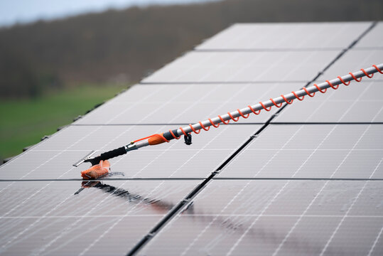 Cleaning a photovoltaic system with a telescopic washing brush and water
