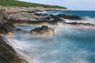 Long exposure shoot of sea waves crashing on seashore and rocks seascape.