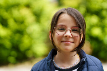 Little cheerful teenage girl wearing glasses outdoors. Happy childhood concept