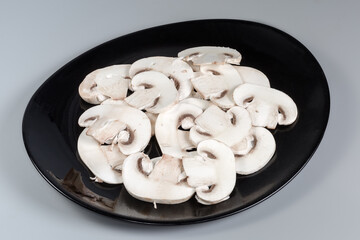Sliced raw button mushrooms on black dish on gray background