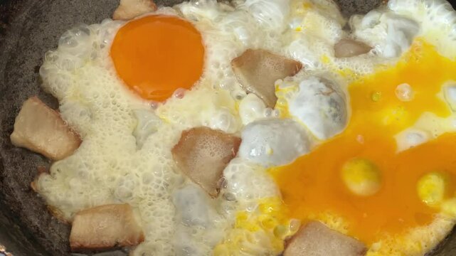 Frying of scrambled eggs with fatback in rustic frying pan