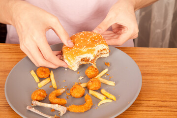 American fast food culture, half-eaten hamburger, potato chips, onion rings and chicken pieces in gray plate on wooden table