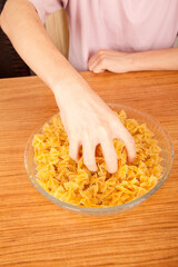 Uncooked raw healthy and pasta macaroni hand held by a Caucasian man, on wooden table in glass plate