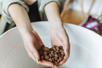 close-up woman's hands pouring expanded clay into flowerpot