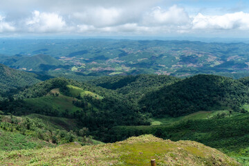 Obraz premium A panoramic summer mountain landscape unfolds with lush green meadows and forests stretching towards majestic peaks under a cloudy sky