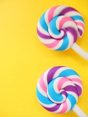 Two colorful lollipops against a yellow background. Vibrant candy pops and space to add...