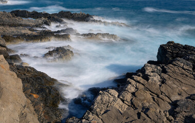 Long exposure shoot of sea waves crashing on seashore and rocks seascape.