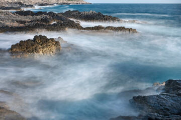 Long exposure shoot of sea waves crashing on seashore and rocks seascape.