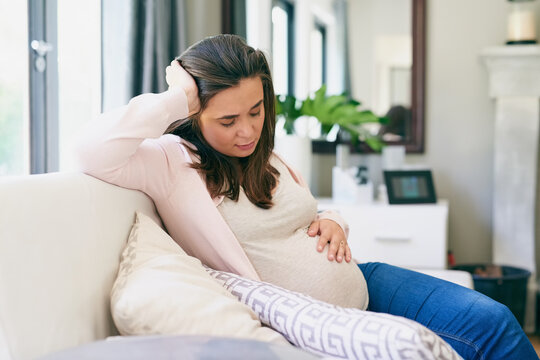 Pregnancy, woman and tired on sofa in home, physical and emotional change for motherhood. Pregnant girl, sleeping and resting on couch for wellness, health and massage belly with hand for comfort